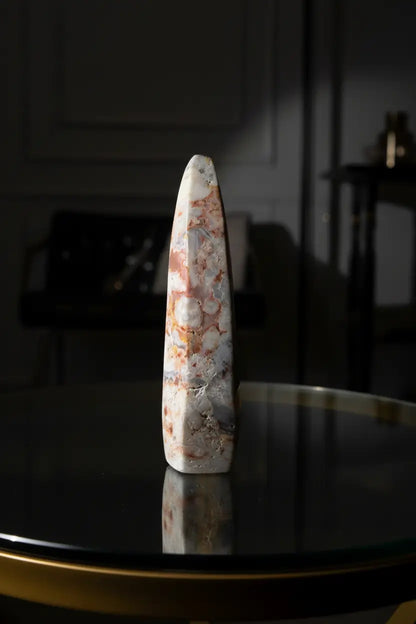 sideview of a crazy lace agate freeform colors are brown, tan, off white freeform is place on a glass top table 
