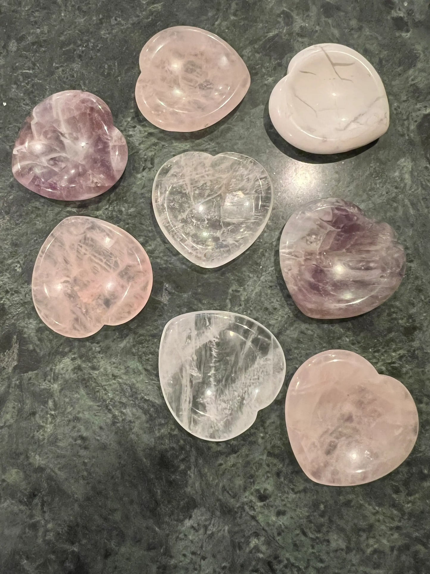 Eight polished, heart-shaped crystals on a green and black marbled surface.