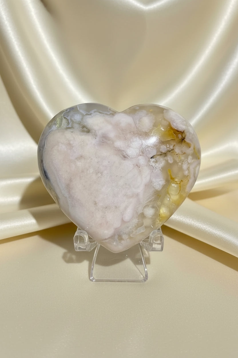close up of flower agate hand carved heart on a stand with a shiny fabric behind 