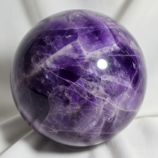 close up amethyst sphere with fractures, beautiful purples, white and likely hematite inclusions shiny platelets catching the light 