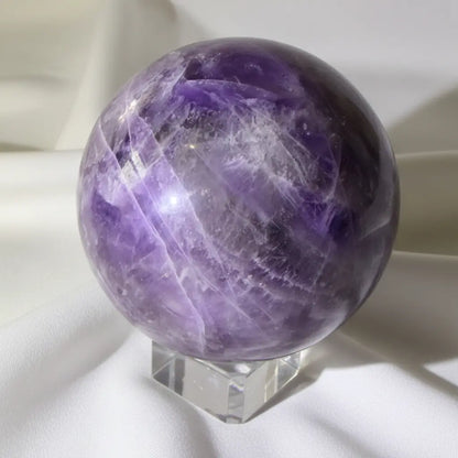 close up amethyst sphere with obvious iron inclusions - Likely hematite and natural fractures purples and white colors white fabric backdrop