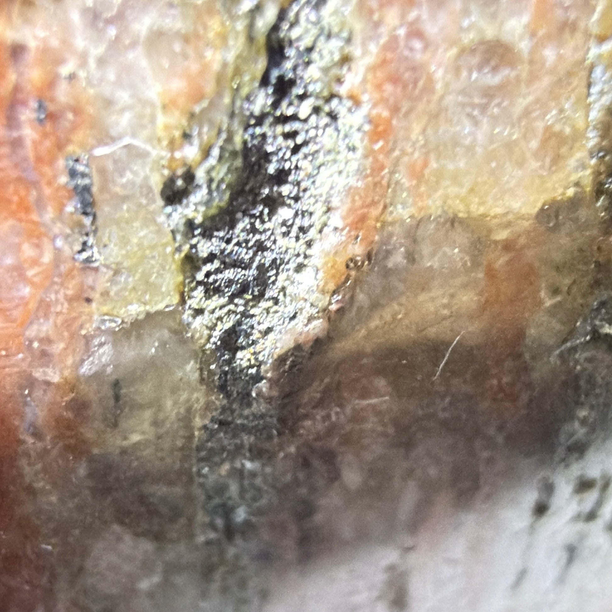A close-up of a rough, textured stone or mineral sample with layered earthy tones including brown, orange, gray, and white.