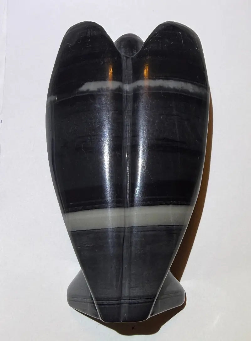 Product photo back of TaiChi Jasper carved angel with a white background.  colors black, gray light and dark, off white bands 