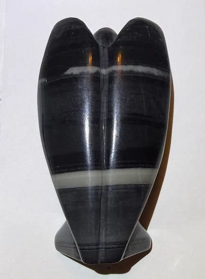 Product photo back of TaiChi Jasper carved angel with a white background.  colors black, gray light and dark, off white bands 