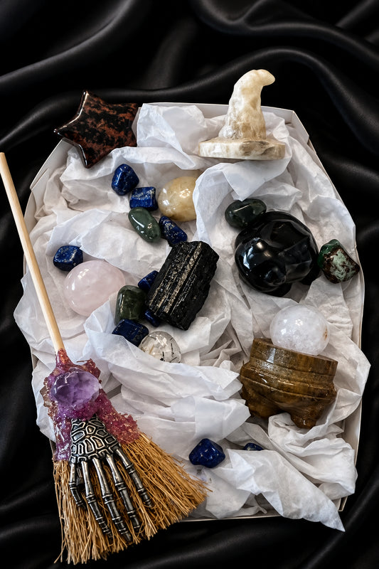 close up contents of set, black obsidian frog, black tourmaline, mahagony obsidian star, calcite witch hat and book with amethyst charm