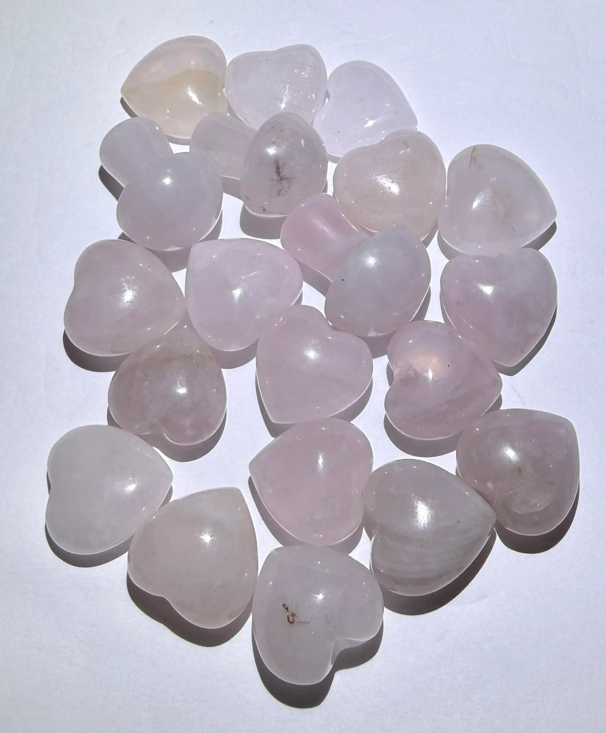 A pile of heart-shaped rose quartz gemstones with smooth, polished surfaces, arranged on a plain white background.