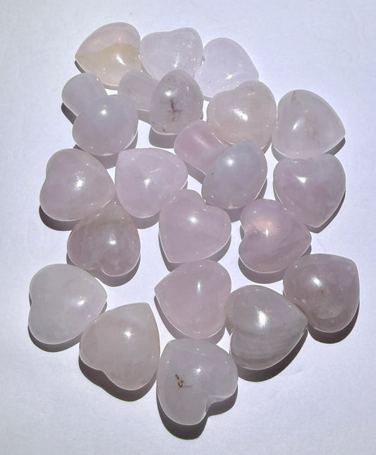 A pile of heart-shaped rose quartz gemstones with smooth, polished surfaces, arranged on a plain white background.