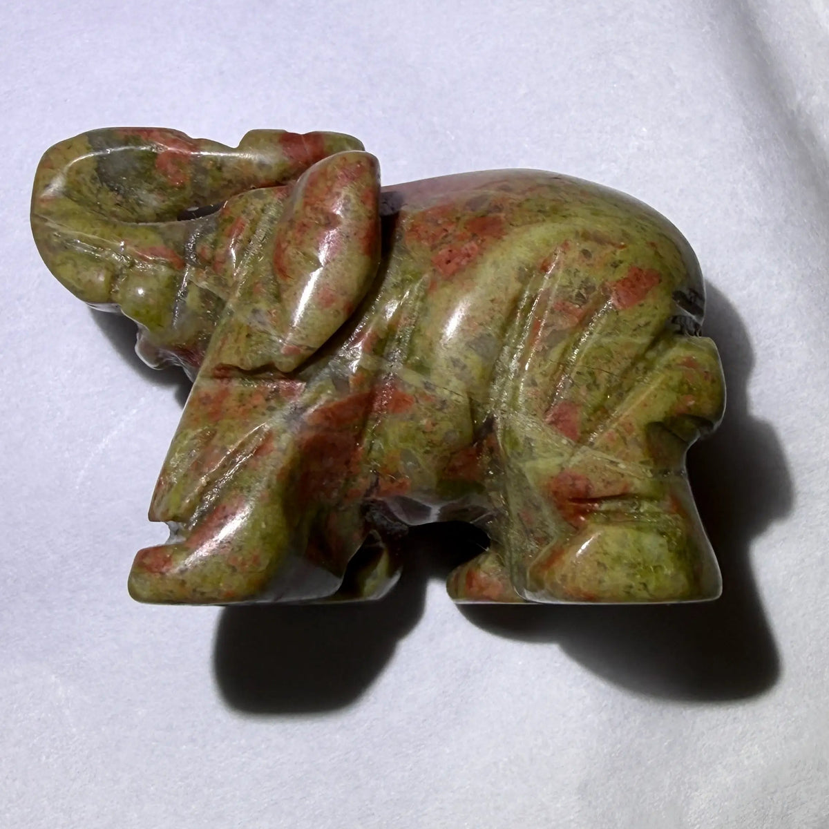close up of small hand carved unakite crystal elephant with trunk up for good luck