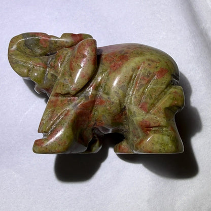 close up of small hand carved unakite crystal elephant with trunk up for good luck