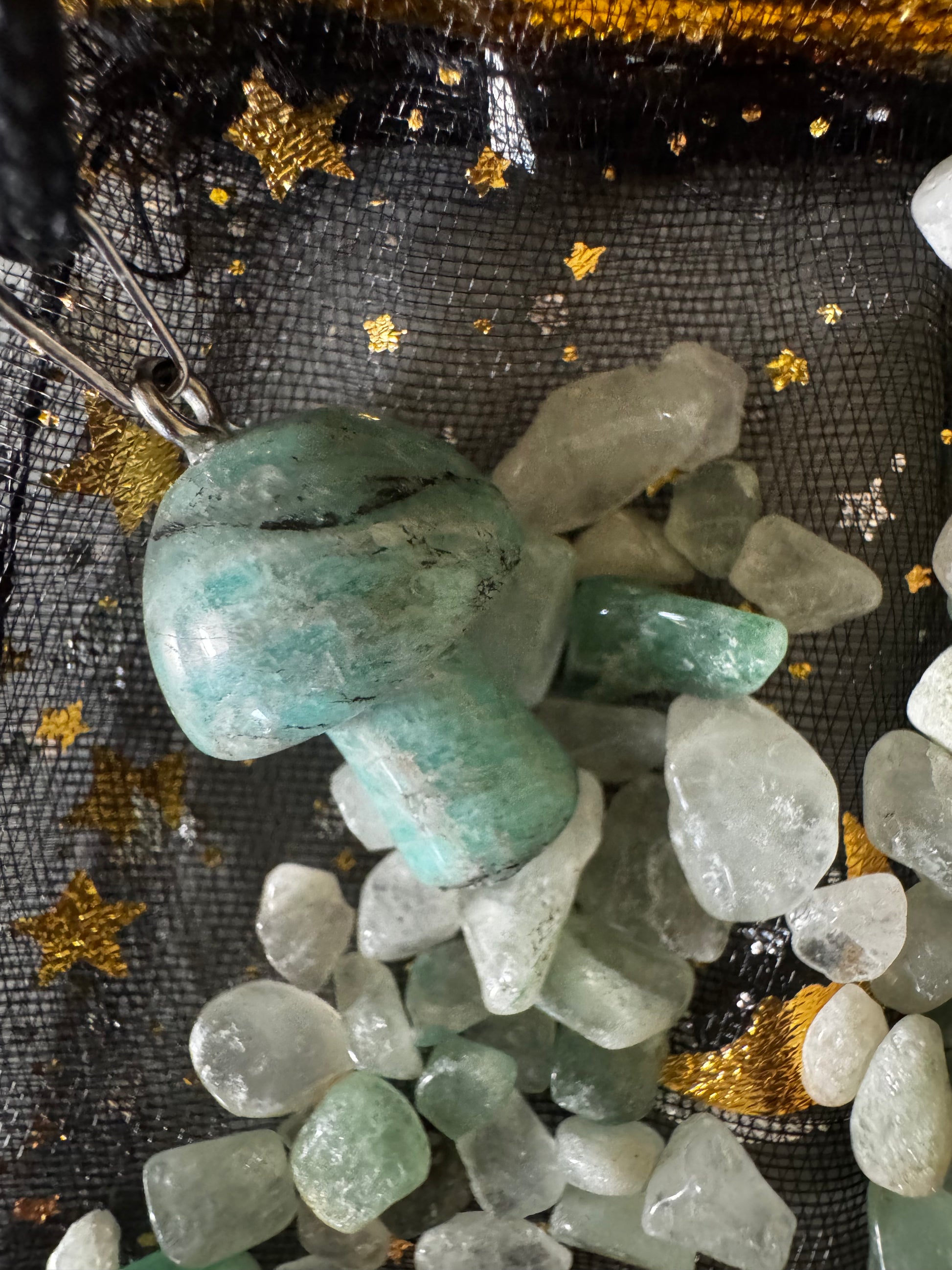 A turquoise mushroom pendant on a black star-patterned mesh with tumbled rocks.