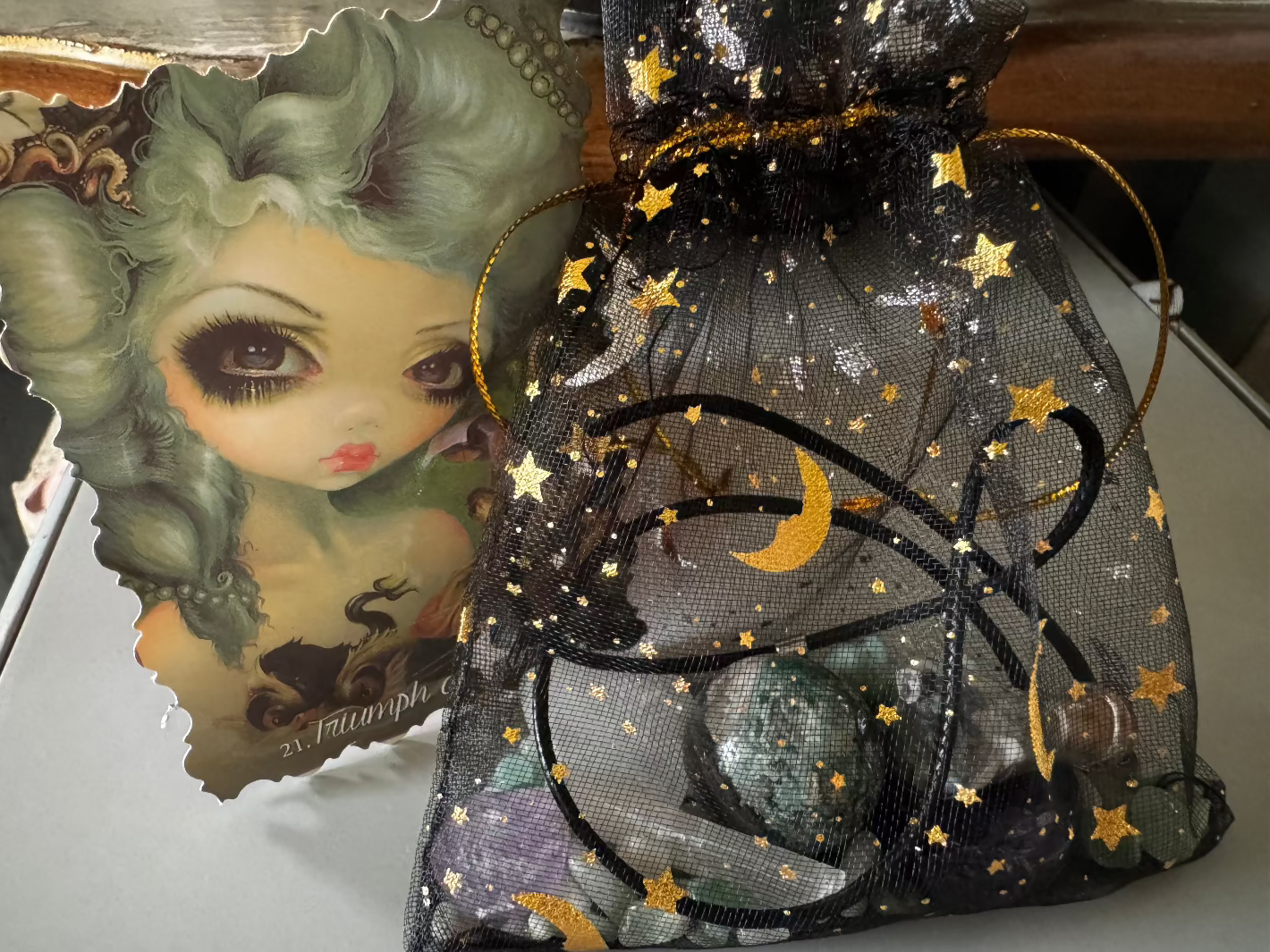 A decorative image of a doll card next to a black, sheer, drawstring bag with gold stars, a gold moon, and black circles.