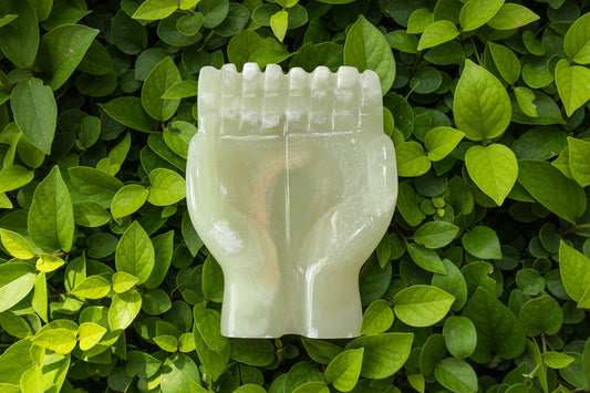 Green onyx offering hands sculpture on a bed of green leaves