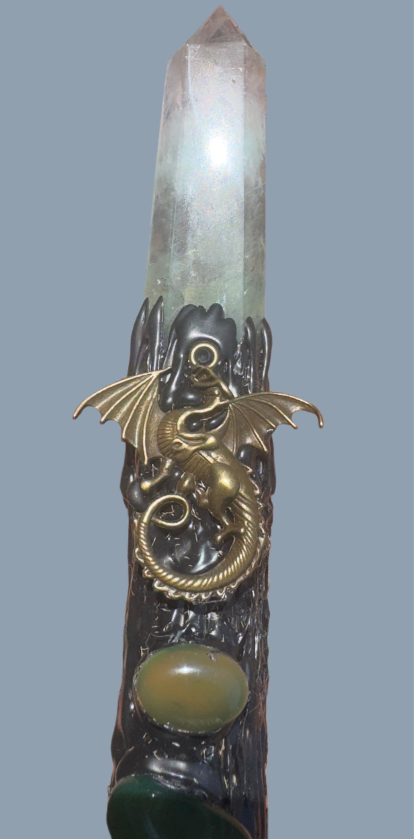 Close-up of a crystal wand with a bronze dragon figurine and green gemstones.
