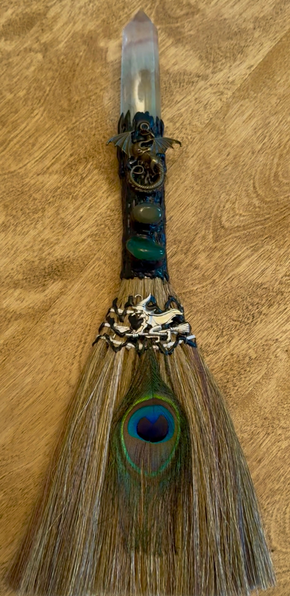 Handcrafted witch broom with crystal, dragon, witch figurine, and peacock feather.
