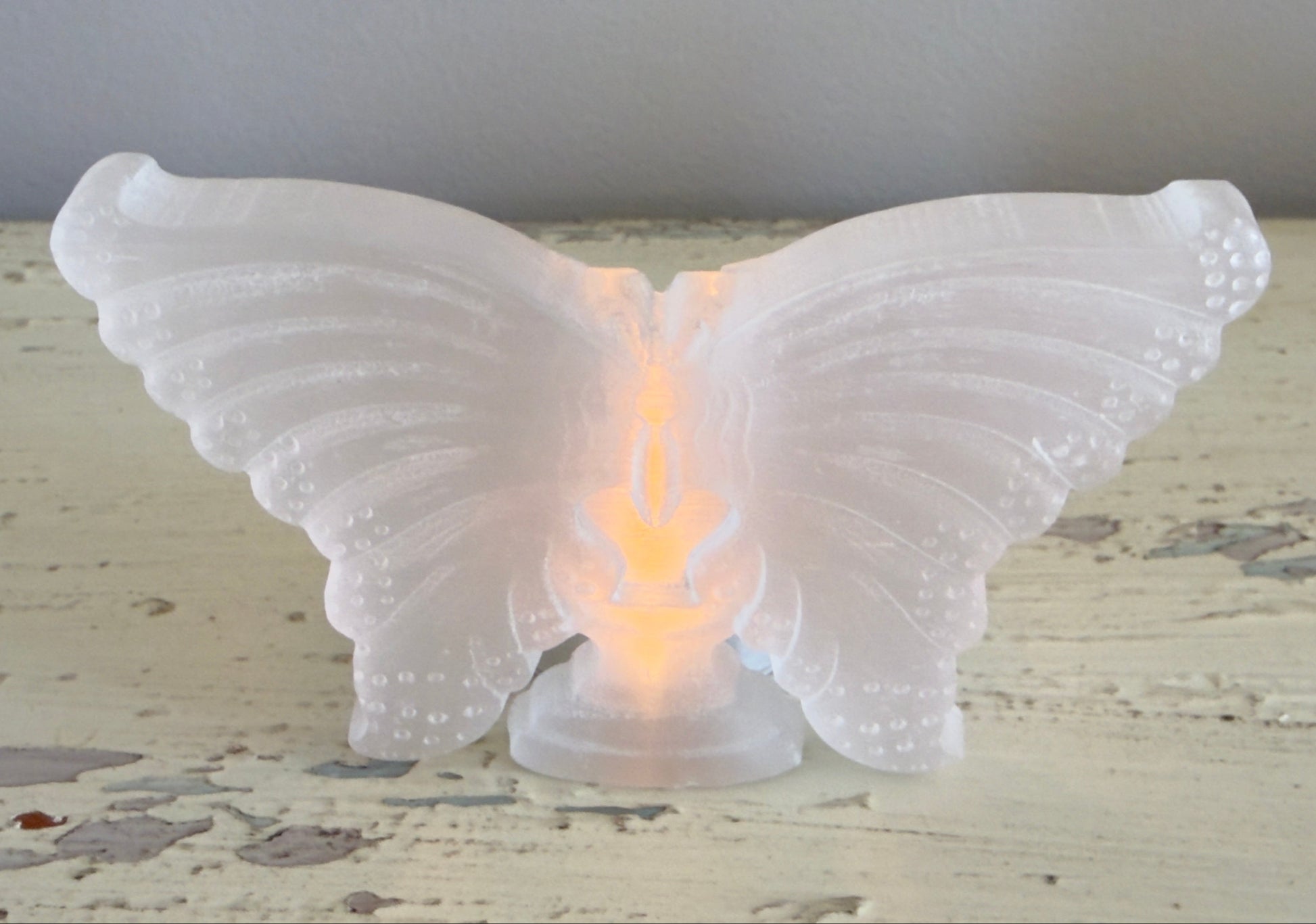 hand carved satin spar butterfly with a lit candle behind it 