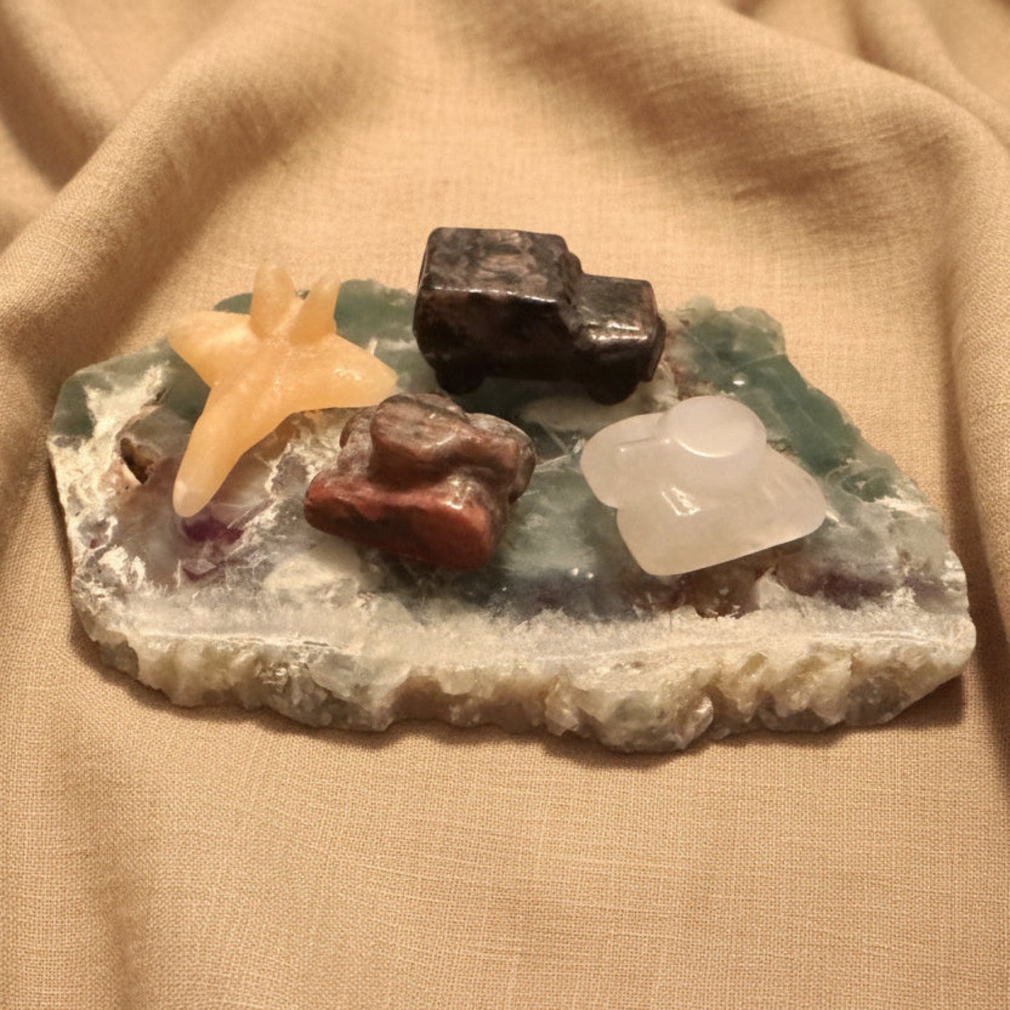 photo of four hand carved pieces, two tanks, clear quartz with citrine inclusion, brecciated jasper, yellow calcite jet, and yooperlite jeep truck  all on a fluroite slab 