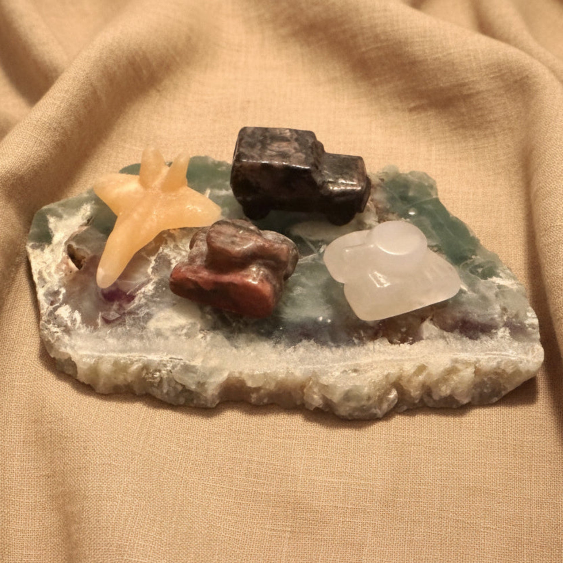 photo of four hand carved pieces, two tanks, clear quartz with citrine inclusion, brecciated jasper, yellow calcite jet, and yooperlite jeep truck  all on a fluroite slab 