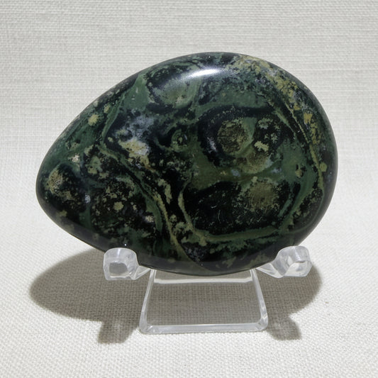 close up of beautiful green with black kambaba jasper worry stone on a clear stand 