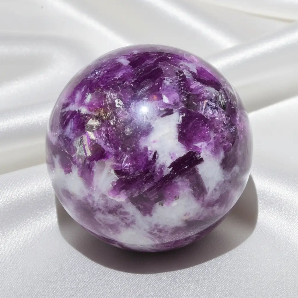 A polished lepidolite crystal sphere with prominent purple and white fluorite inclusions 