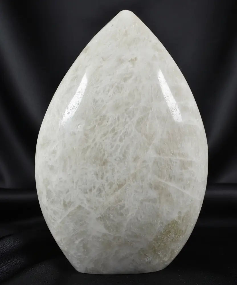 A teardrop-shaped moonstone polished  sculpture with a creamy off-white color and natural fibrous crystalline texture 