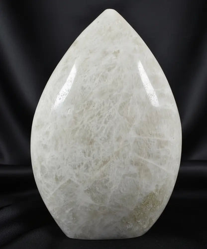 A teardrop-shaped moonstone polished  sculpture with a creamy off-white color and natural fibrous crystalline texture 