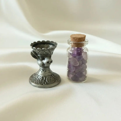 close up of brass chinese zodiac pig sphere holder and a glass wish bottle with amethyst chips 