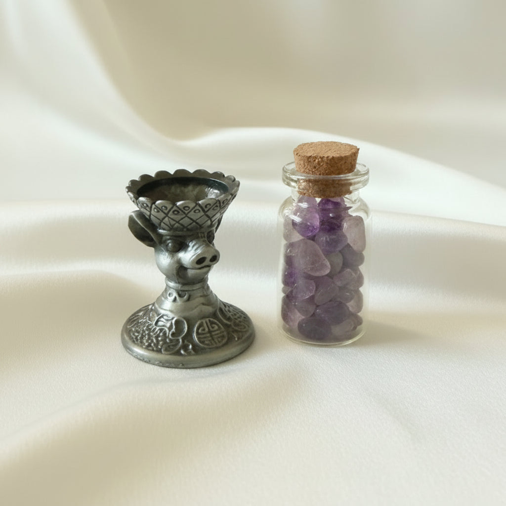 close up of brass chinese zodiac pig sphere holder and a glass wish bottle with amethyst chips 
