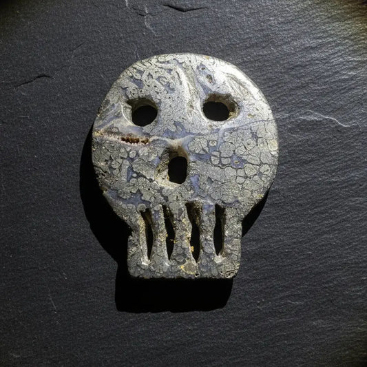 A carved pyrite skull-shaped object with eye and mouth cutouts