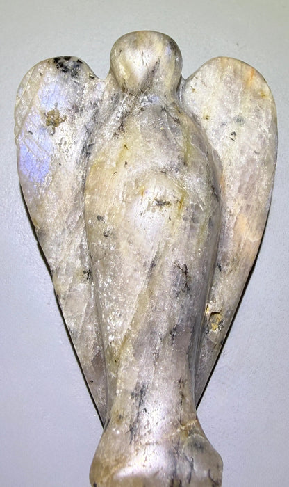 A carved angel figurine made of moonstone, showing a natural adularescence blue on the left wing and gray, beige, and brown veining throughout.