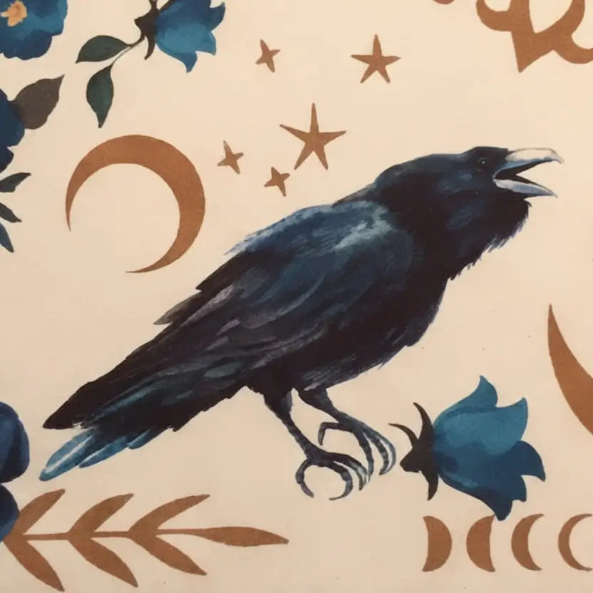 A close-up of a cream-colored fabric or paper print featuring a black raven in profile, blue flowers, brown crescent moons, and brown ornamental scrollwork.
