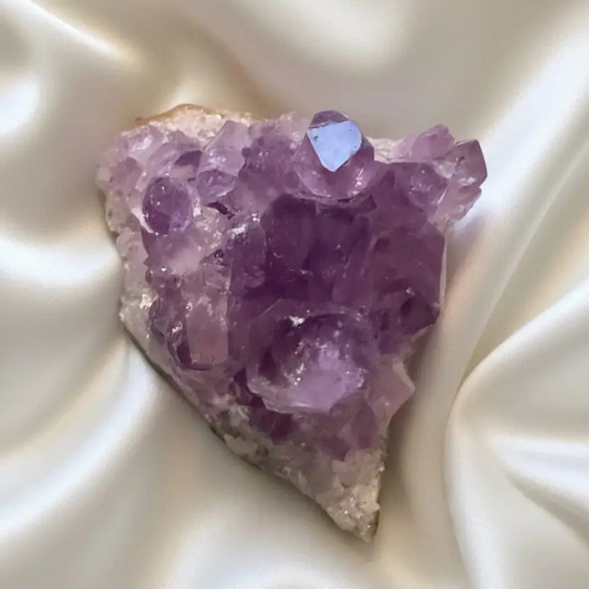 A raw amethyst crystal cluster with purple crystalline formations on a rough white matrix, displayed on a beige surface.
