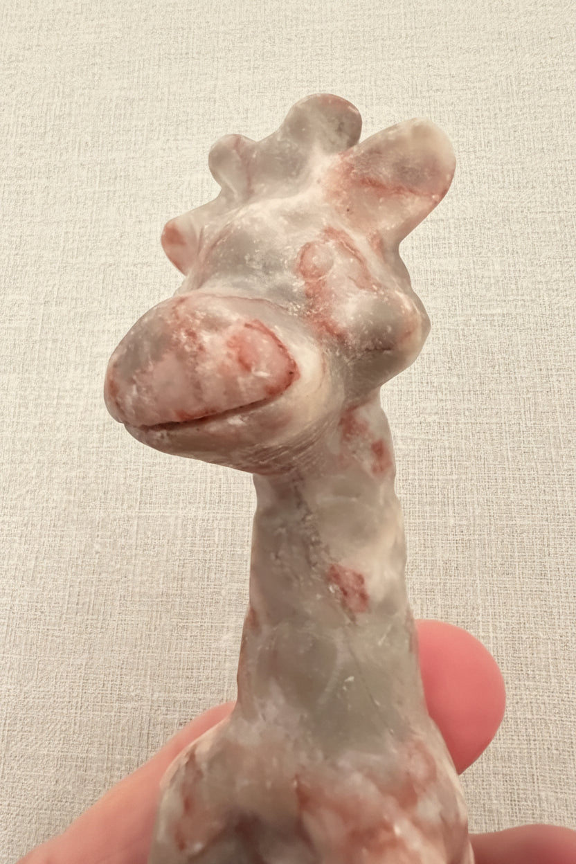 close up carving red vein jasper giraffe. Cute facial details dark pink colors weave through the jasper 