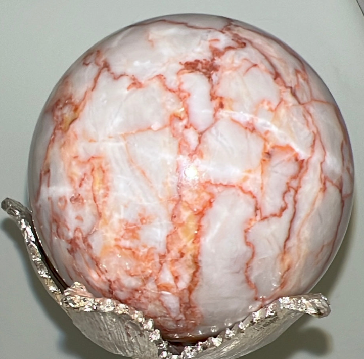 Close up Red Vein Jasper Sphere off white with orange/red veins in a silver stand 