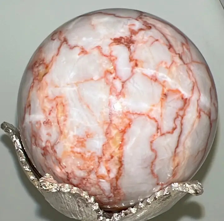 Close up Red Vein Jasper Sphere off white with orange/red veins in a silver stand 