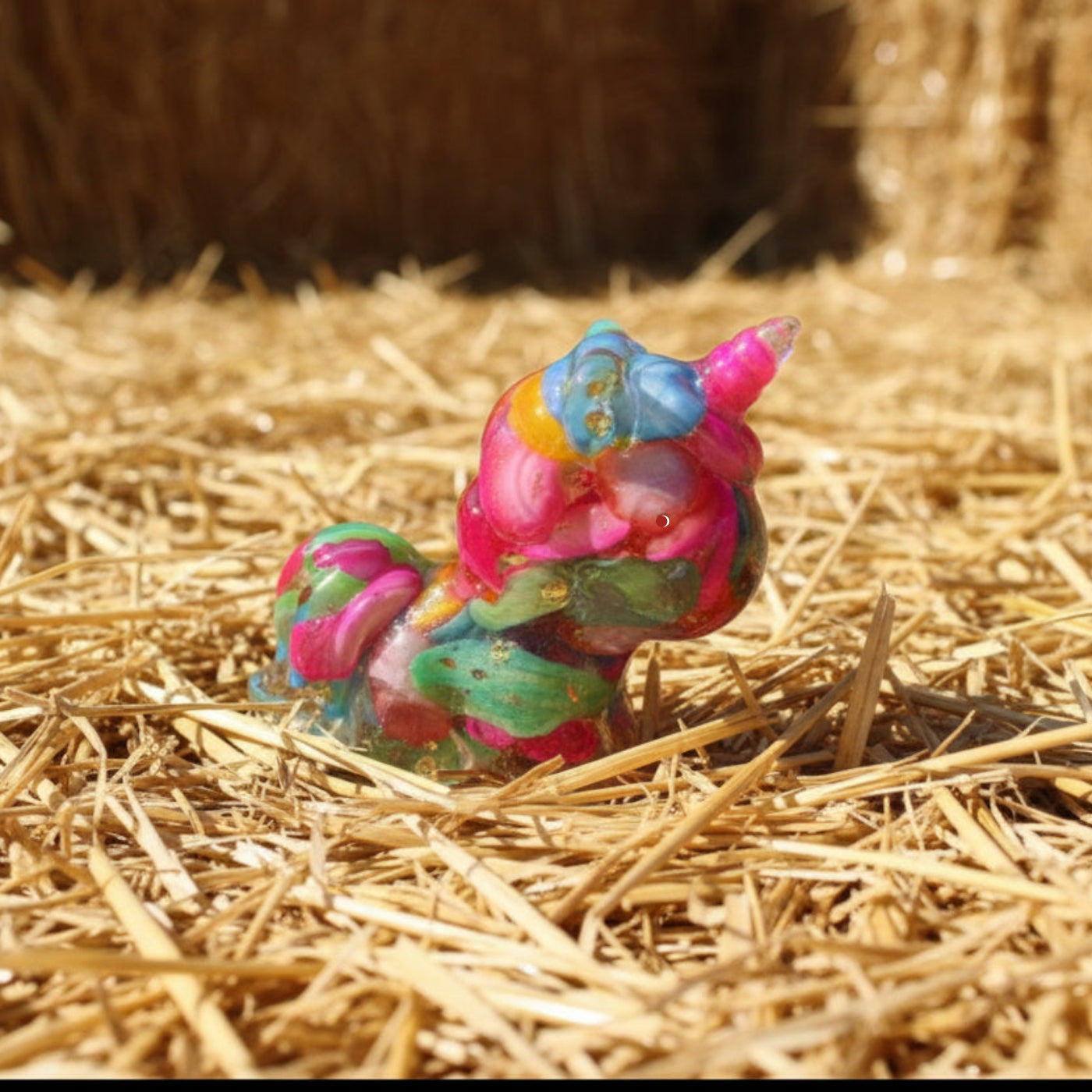 A little resin unicorn filled with carnival colors bright blue, yellow, pink, green dyed agate or stone sitting on a bed of straw. Product has gold toned metal shavings - orgonite like 