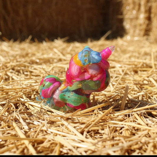 A little resin unicorn filled with carnival colors bright blue, yellow, pink, green dyed agate or stone sitting on a bed of straw. Product has gold toned metal shavings - orgonite like 