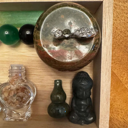 Wooden box with small crystals, glass heart bottle, and a tiny Buddha statue.