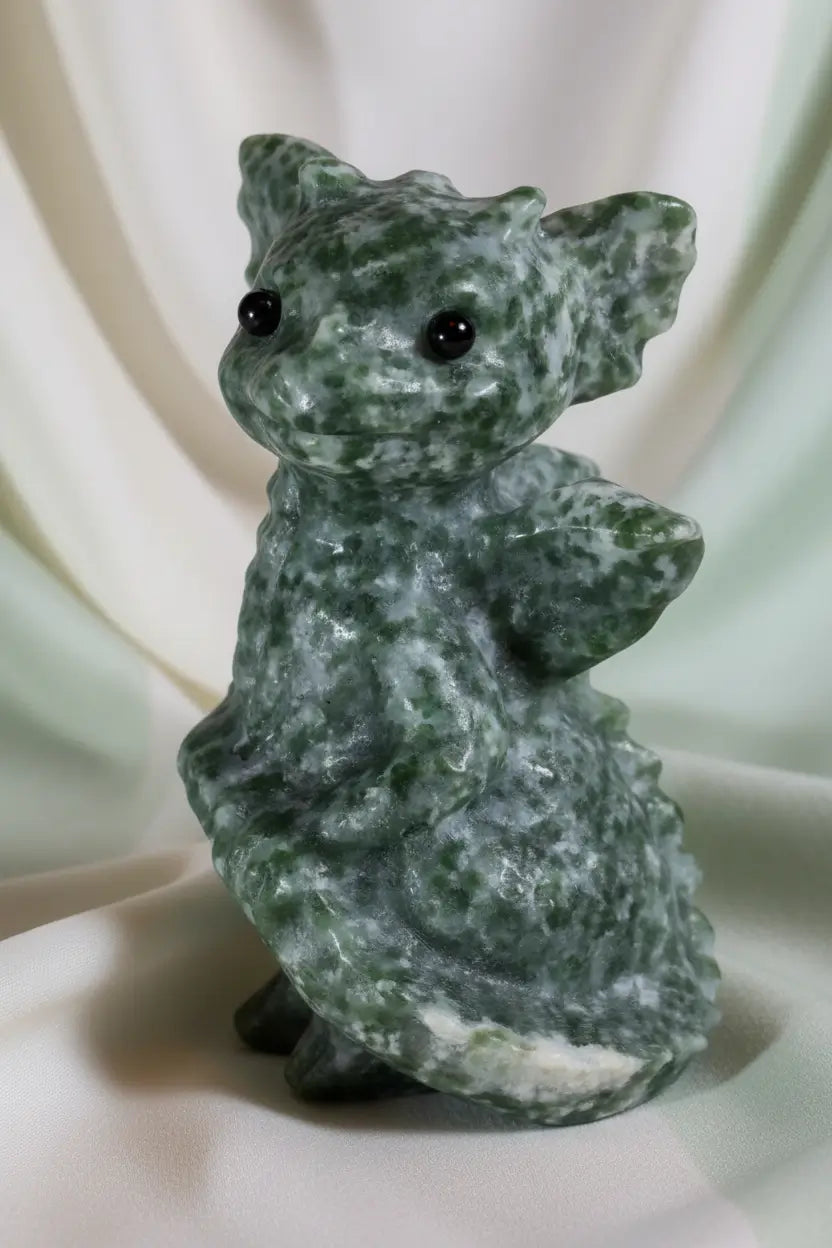 baby dragon carved from tree agate deep greens, off white speckles, with a soft off white background 