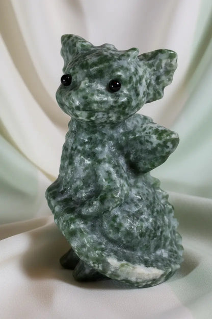 baby dragon carved from tree agate deep greens, off white speckles, with a soft off white background 