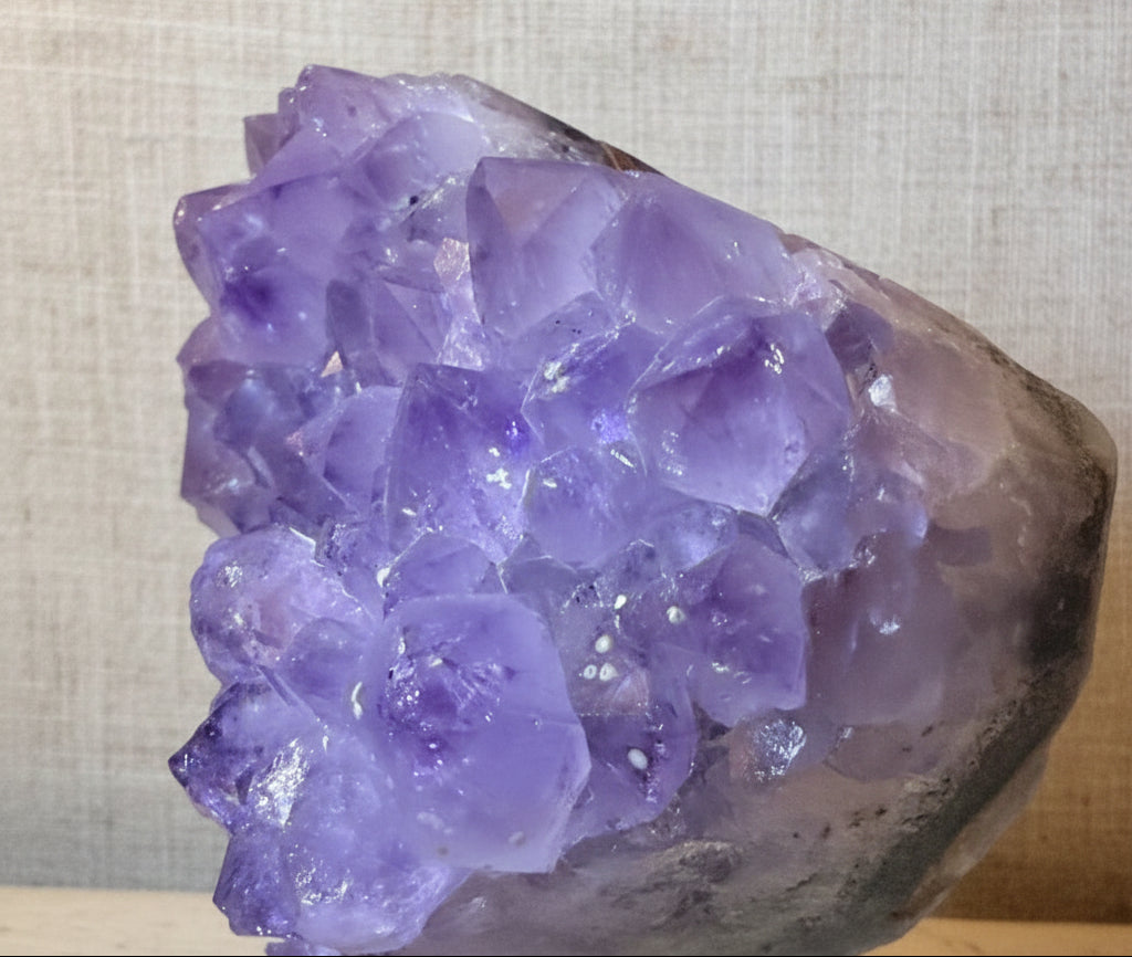 A purple amethyst crystal cluster mounted on a clear acrylic display stand, photographed close-up against a light neutral background.