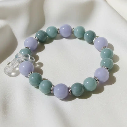 A close-up of an aventurine and angelite, clear quartz beaded bracelet  separated by small silver spacer rings, includes a silvery bell. 