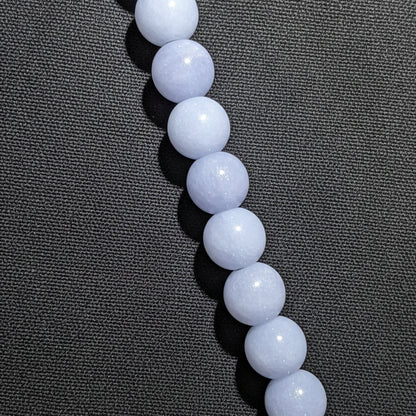 A close-up of a strand of smooth, Angelite blue-gray round beads, likely arranged vertically on a black surface