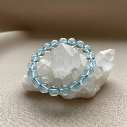 A beaded stretch bracelet made of light blue round glass beads, displayed on a white crystal cluster against a soft beige background.