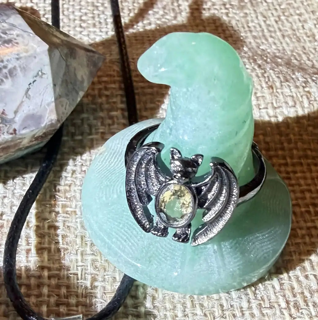 close up of green aventurine carved hat with bat ring, and tip of tower all with a burlap fabric background