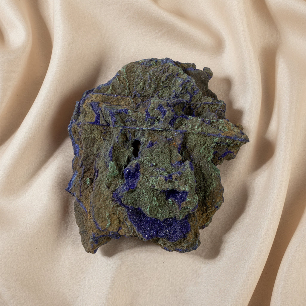 A raw azurite mineral specimen showing a textured brown matrix with vibrant purple and green metallic deposits 
