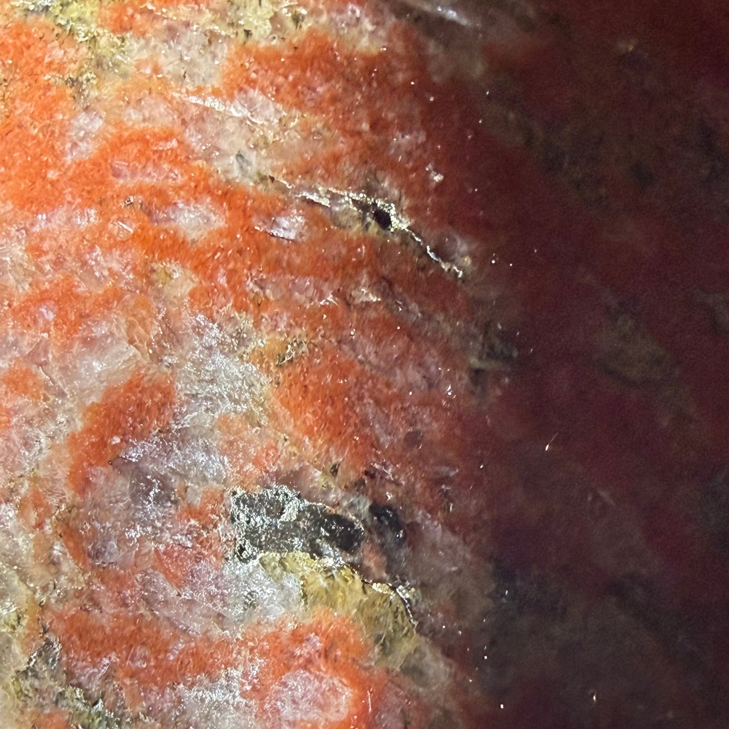 A close-up of a polished jasper crystal with a mottled pattern of orange, red, cream, and dark brown, resting on a white surface.