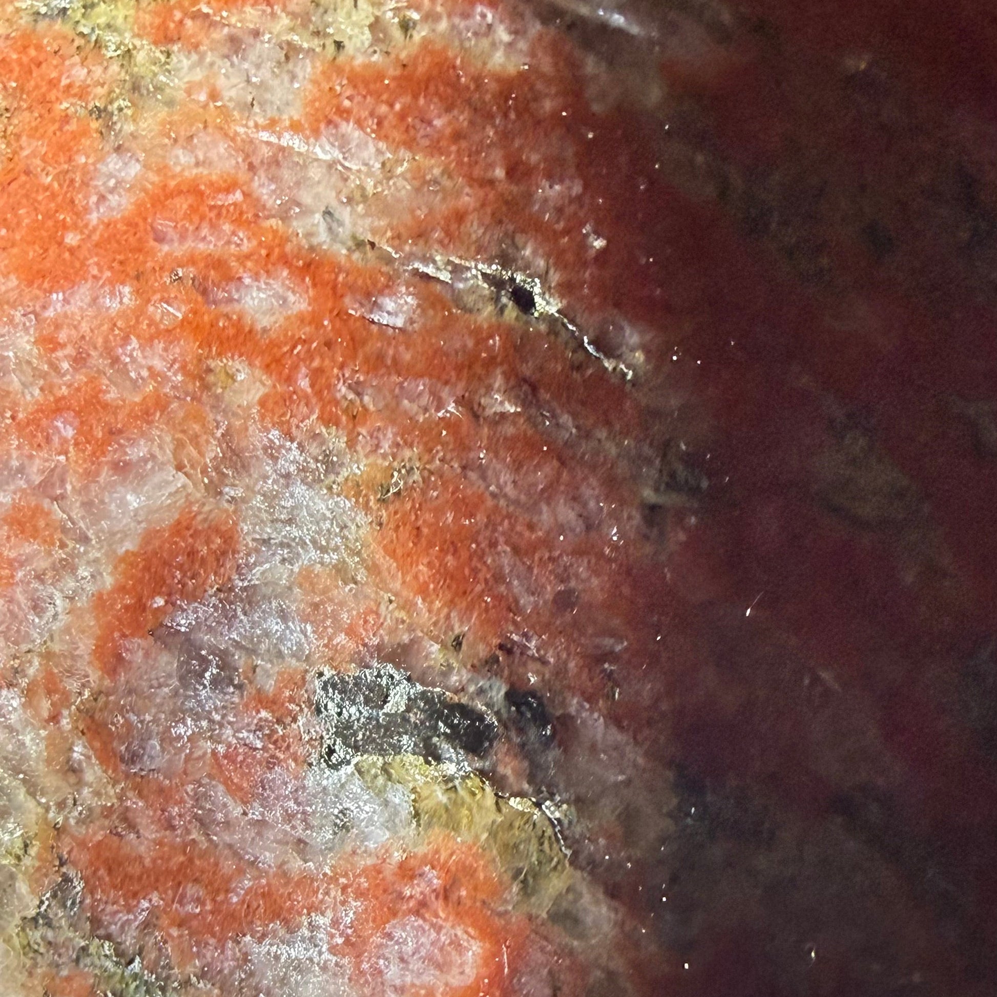 A close-up of a polished jasper crystal with a mottled pattern of orange, red, cream, and dark brown, resting on a white surface.