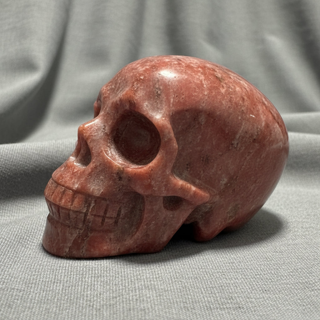 A polished red jasper skull figurine resting on a light-colored surface  