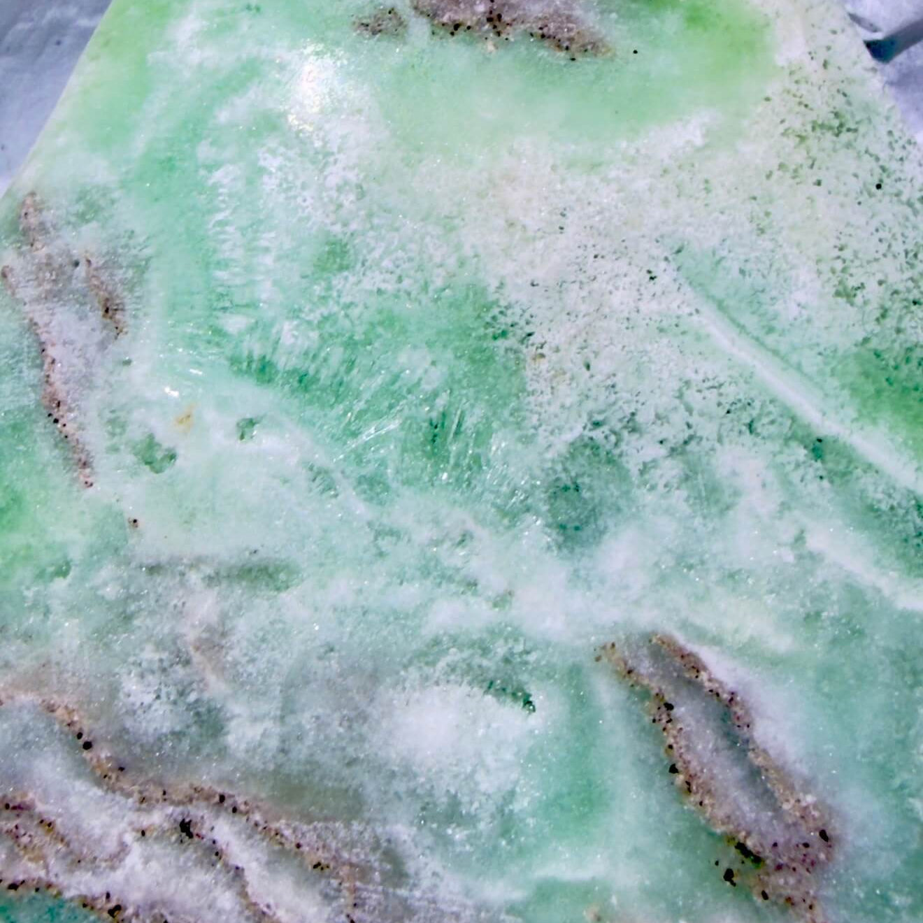 A close-up of a Caribbean Calcite freeform showing the calcite rosettes, and aragonite banding beautiful ocean greens and soft, warm browns 