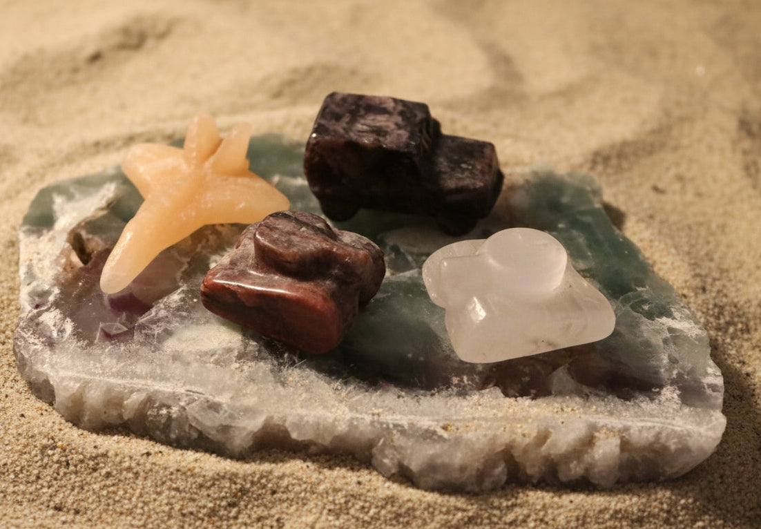 photo of four hand carved pieces, two tanks, clear quartz with citrine inclusion, brecciated jasper, yellow calcite jet, and yooperlite jeep truck  all on a fluroite slab 